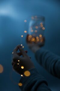 Hands holding a jar with glowing lights, creating a magical atmosphere at night.